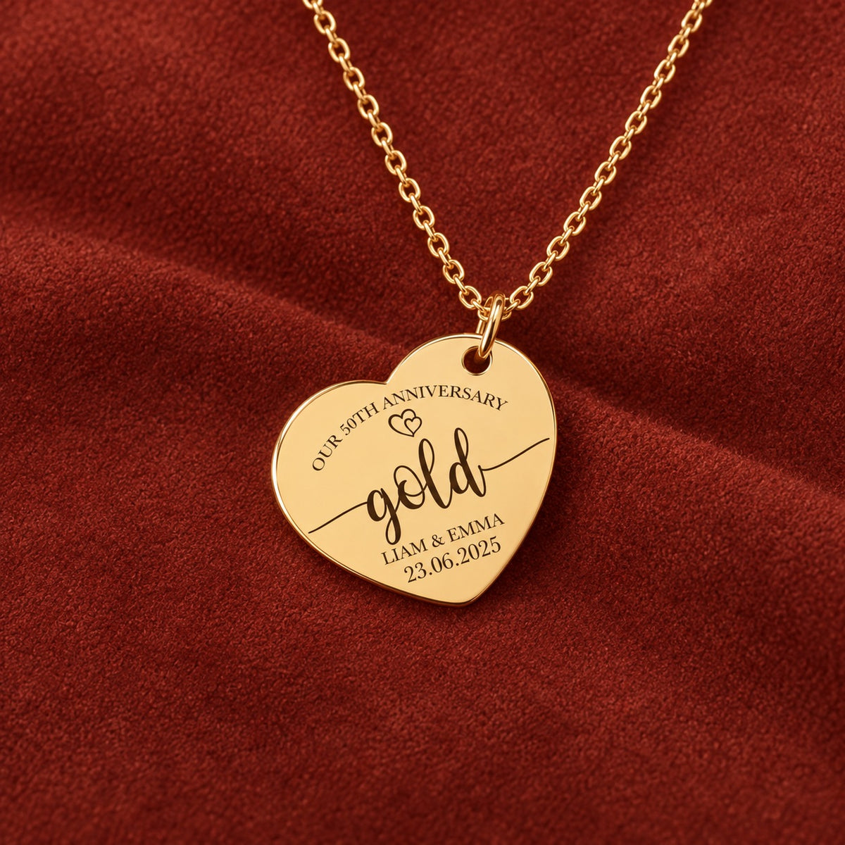 Médaille en cœur dorée avec inscription « gold », prénoms Liam et Emma et date 23.06.2025, sur suédine rouge sanguine.