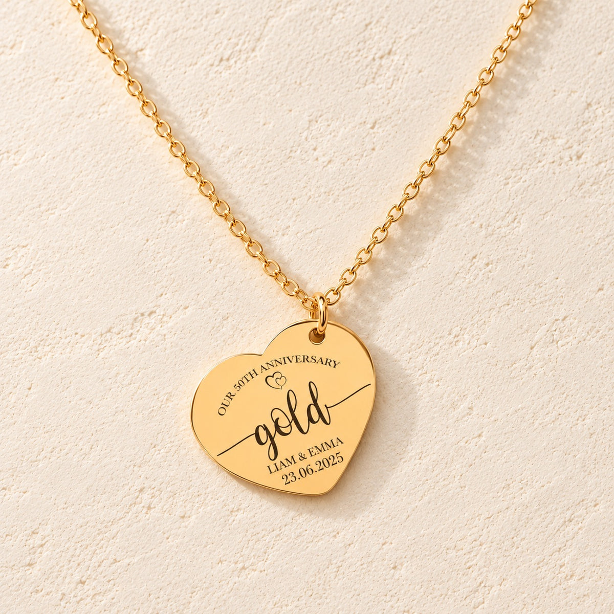 Collier Coeur Anniversaire de Mariage 50 ans doré, médaille en cœur gravée avec inscription « gold », prénoms Liam et Emma et date 23.06.2025, sur fond ivoire.