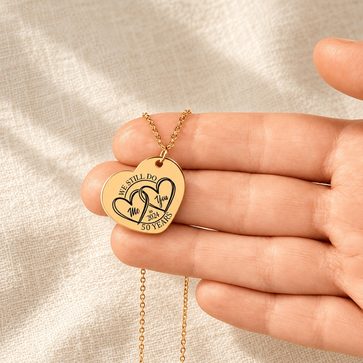 Collier Coeur Anniversaire de Mariage 50 ans doré tenu en main, détail de la gravure.