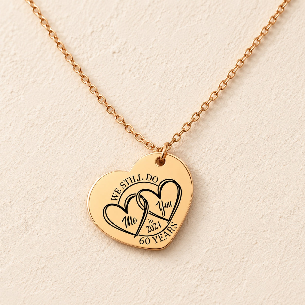 Collier cœur anniversaire de mariage 60 ans doré, médaille en cœur gravée avec deux cœurs et inscription « 60 YEARS », sur fond ivoire.