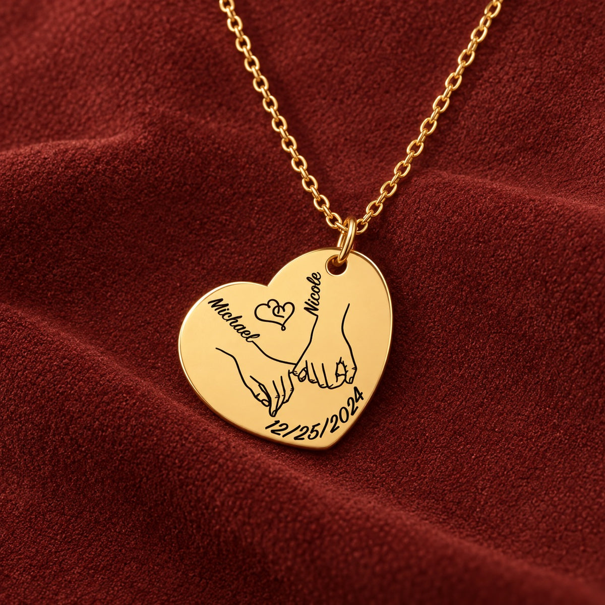 Médaille en cœur dorée avec deux mains liées, prénoms Michael et Nicole et date 12/25/2024, sur suédine rouge sanguine.