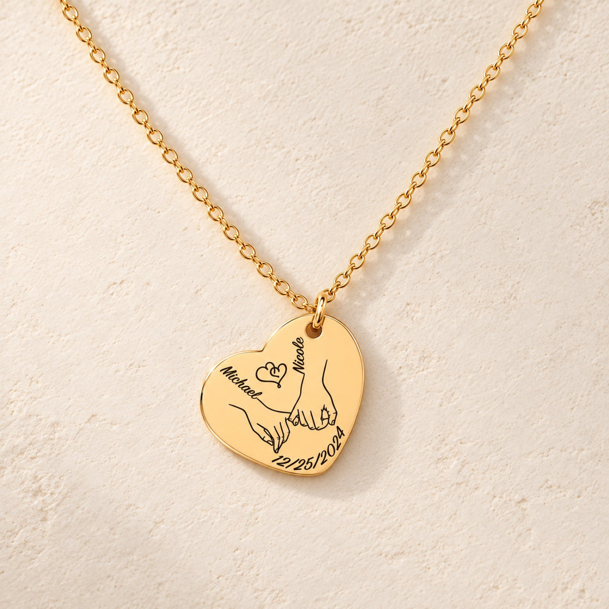 Collier Coeur Notre Premier Noël Ensemble personnalisé doré, médaille en cœur gravée avec deux mains liées, prénoms Michael et Nicole et date 12/25/2024, sur fond ivoire.