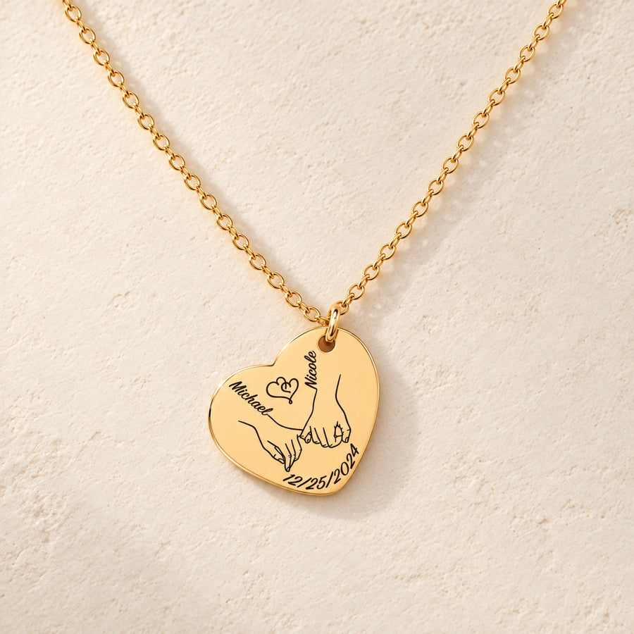 Collier Coeur Notre Premier Noël Ensemble personnalisé doré, médaille en cœur gravée avec deux mains liées, prénoms Michael et Nicole et date 12/25/2024, sur fond ivoire.