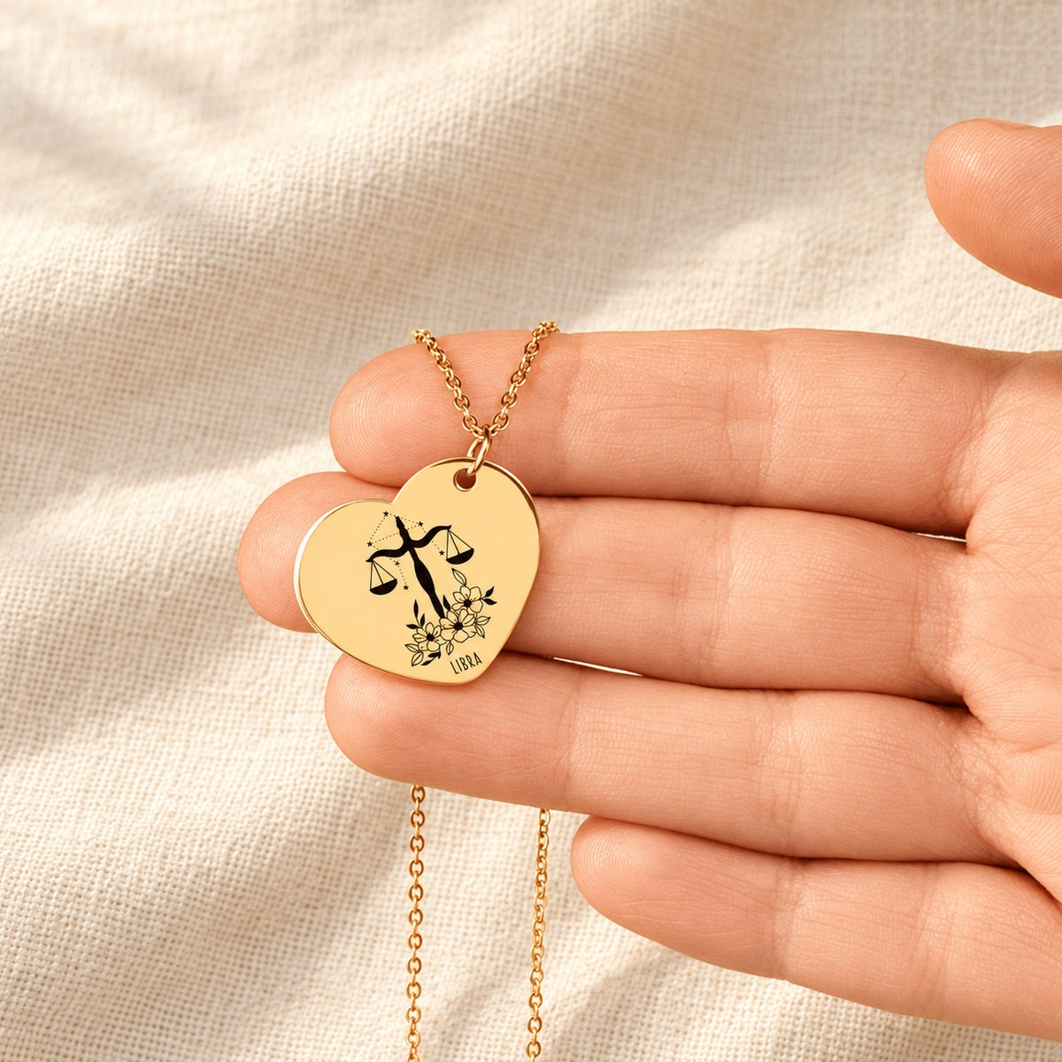 Collier cœur signe astrologique Balance doré tenu en main, détail de la gravure.