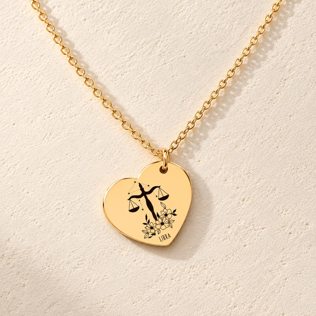 Collier cœur signe astrologique Balance doré, médaille en cœur gravée avec motif du signe Balance et ornements, sur fond ivoire.