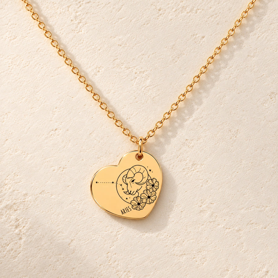 Collier cœur signe astrologique Bélier doré, médaille en cœur gravée avec motif du signe Bélier et ornements, sur fond ivoire.