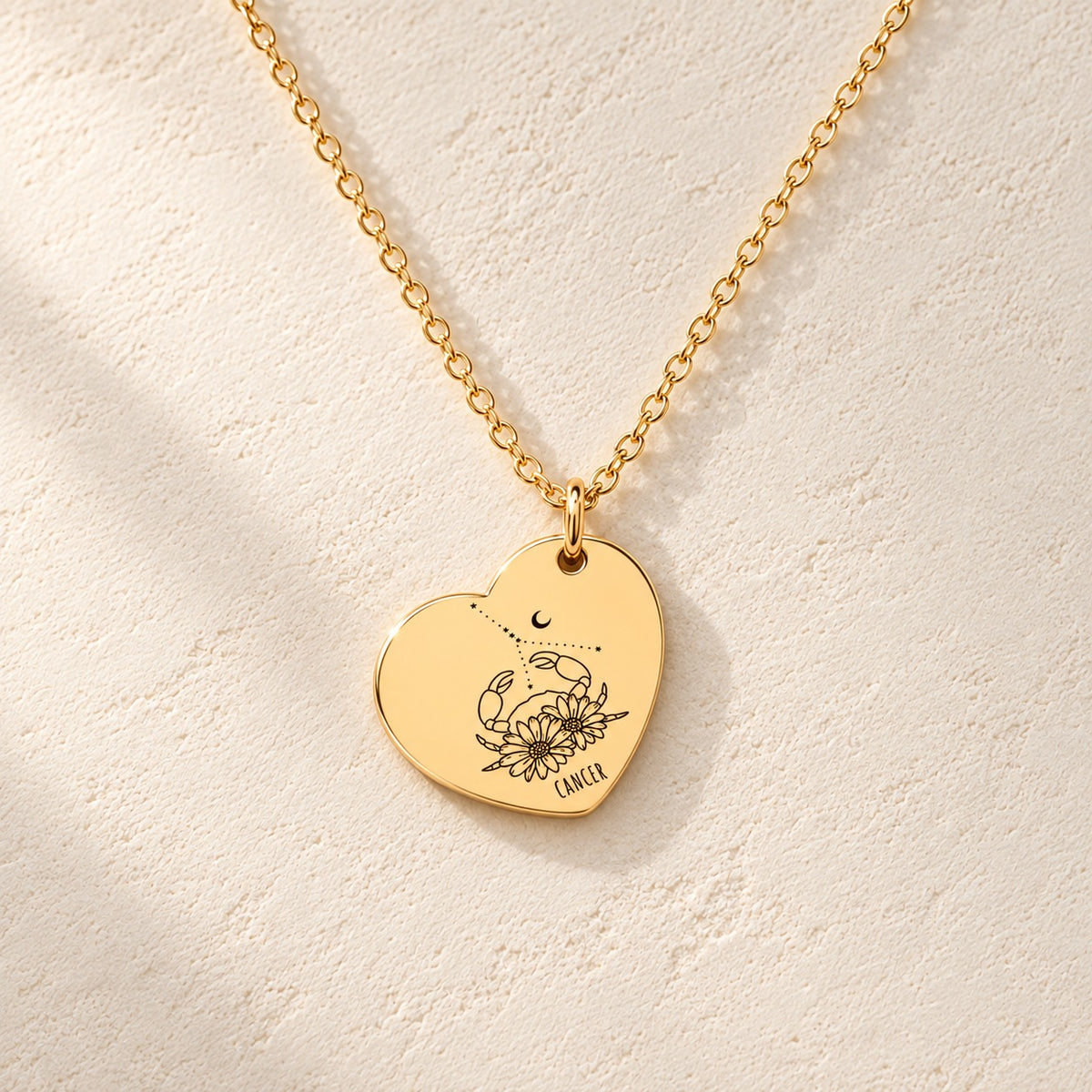 Détail de la médaille en cœur dorée avec motif du signe Cancer et ornements.