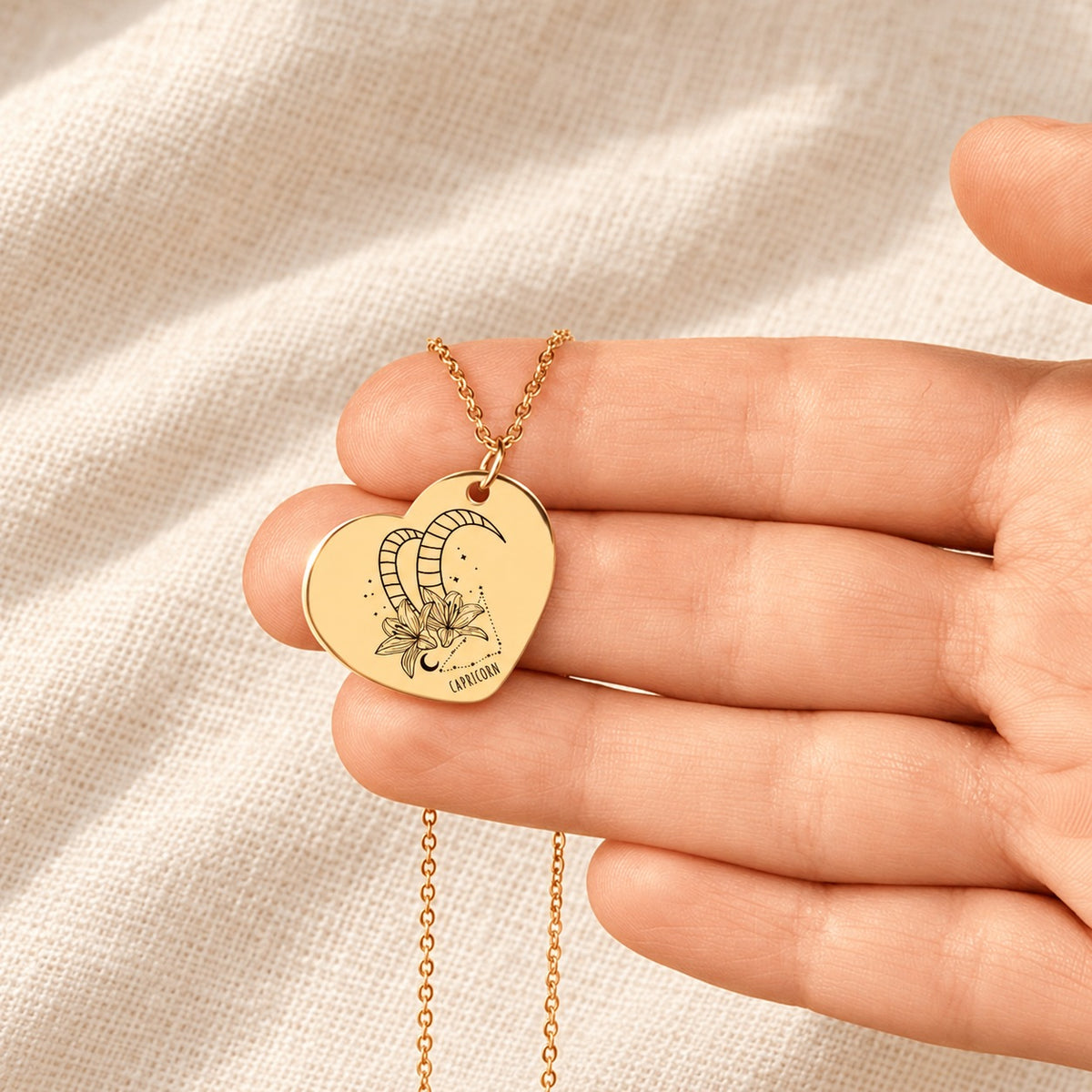 Collier cœur signe astrologique Capricorne doré tenu en main, détail de la gravure.