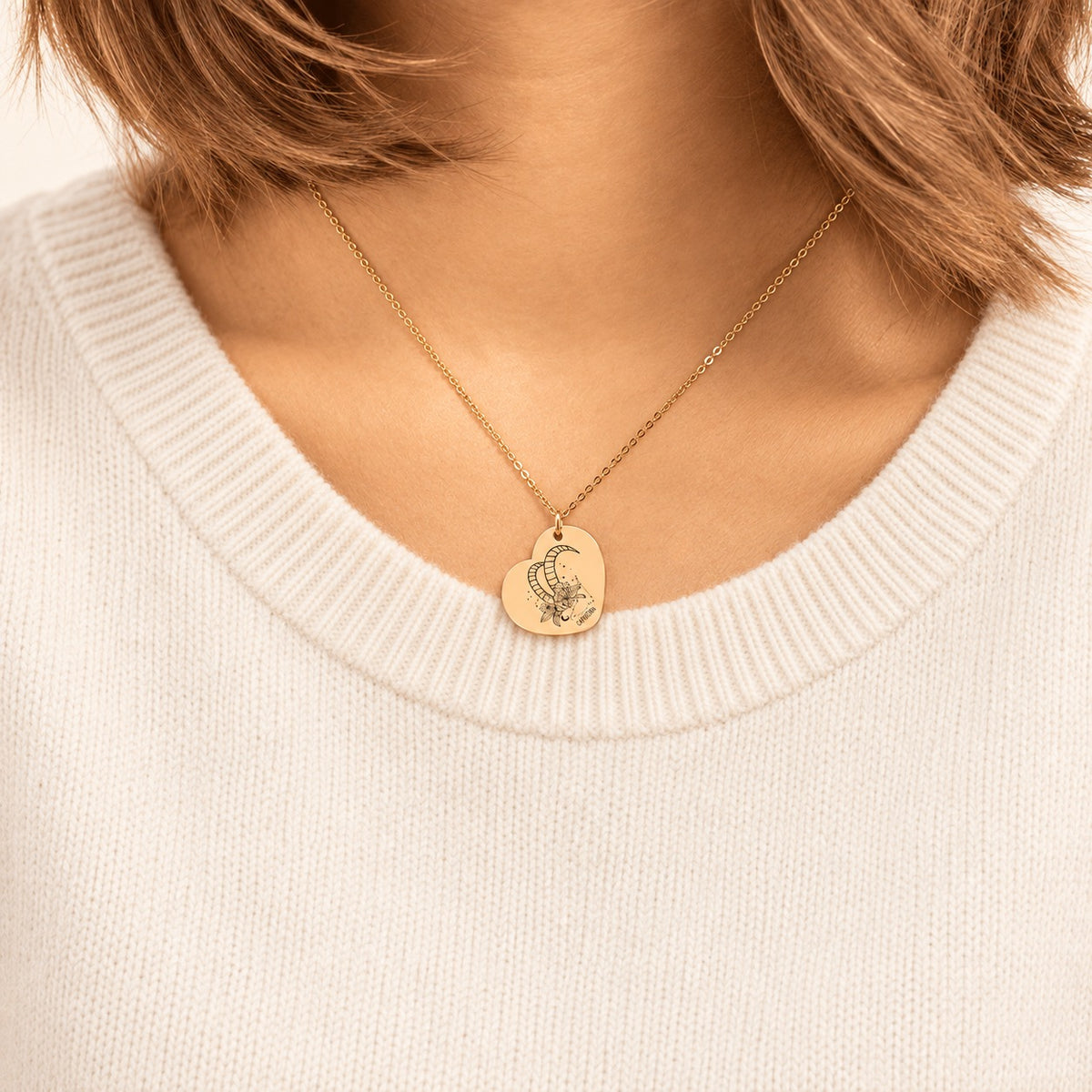 Collier cœur signe astrologique Capricorne doré porté au cou, médaille en cœur gravée.