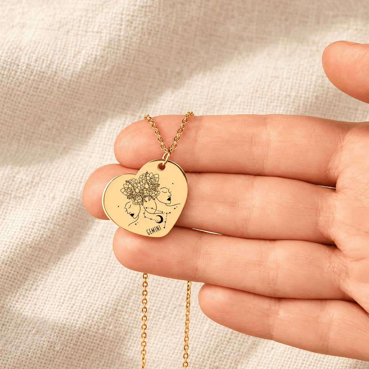 Collier cœur signe astrologique Gémeaux doré tenu en main, détail de la gravure.