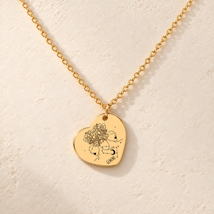 Collier cœur signe astrologique Gémeaux doré, médaille en cœur gravée avec motif du signe Gémeaux et ornements, sur fond ivoire.