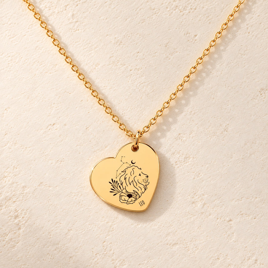 Collier cœur signe astrologique Lion doré, médaille en cœur gravée avec motif du signe Lion et ornements, sur fond ivoire.