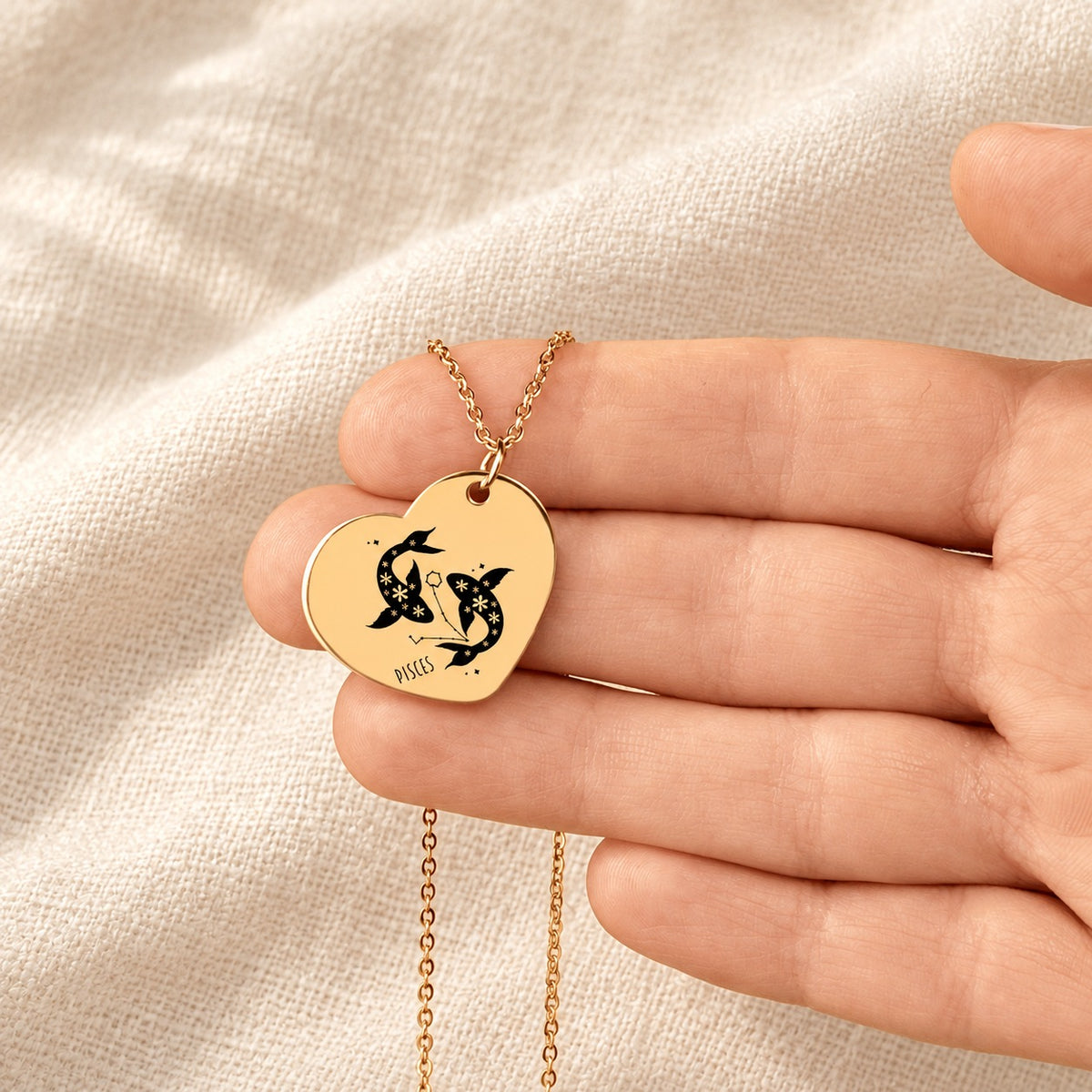 Collier cœur signe astrologique Poissons doré tenu en main, détail de la gravure.