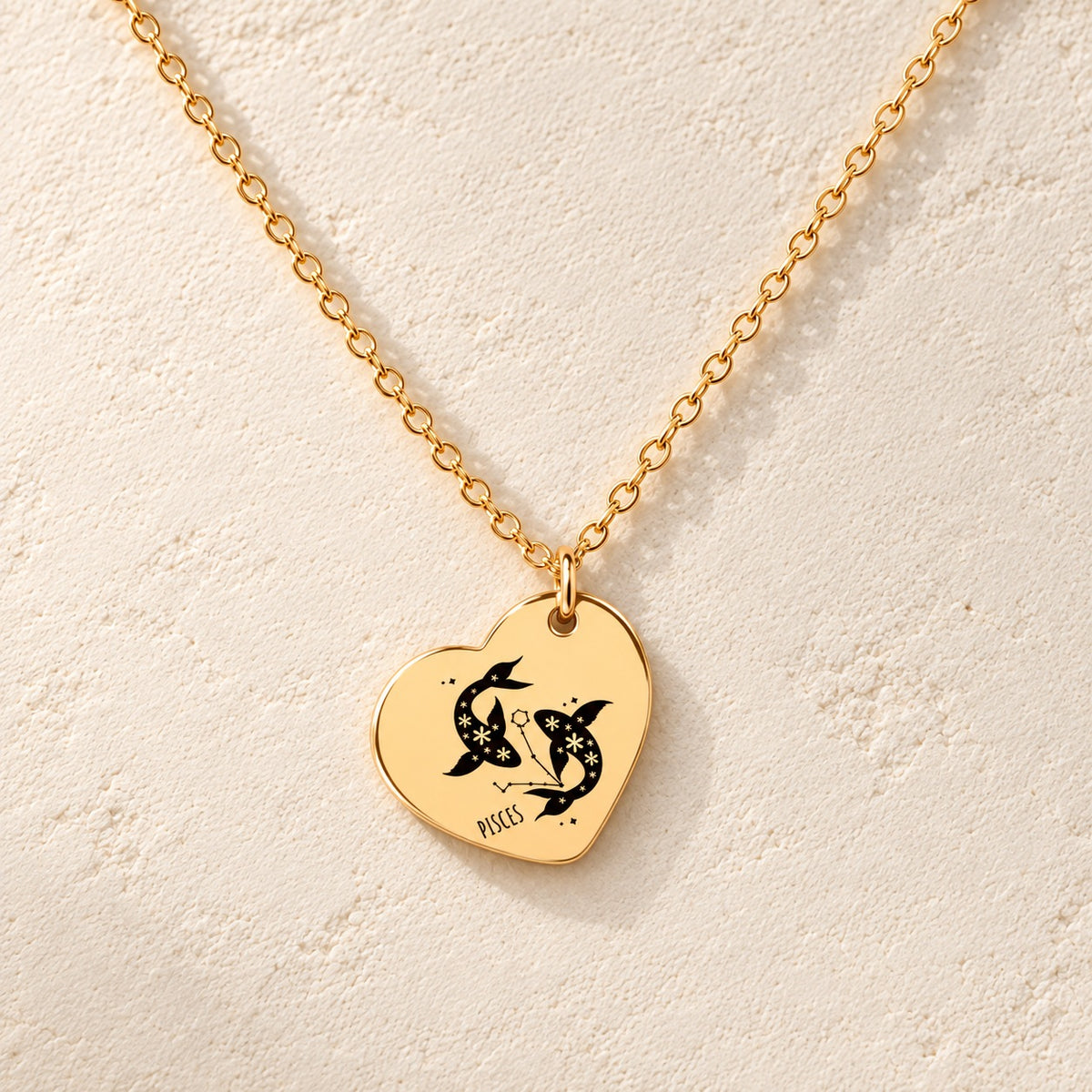Collier cœur signe astrologique Poissons doré, médaille en cœur gravée avec motif du signe Poissons et ornements, sur fond ivoire.
