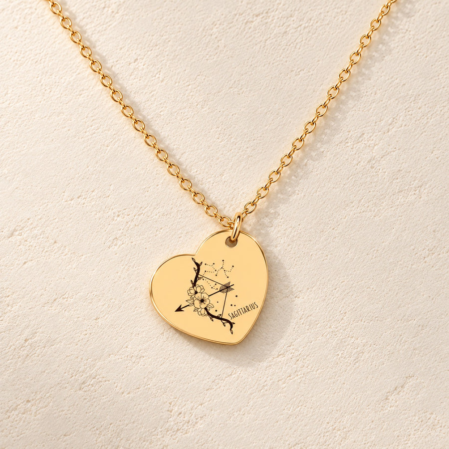Collier cœur signe astrologique Sagittaire doré, médaille en cœur gravée avec motif du signe Sagittaire et ornements, sur fond ivoire.