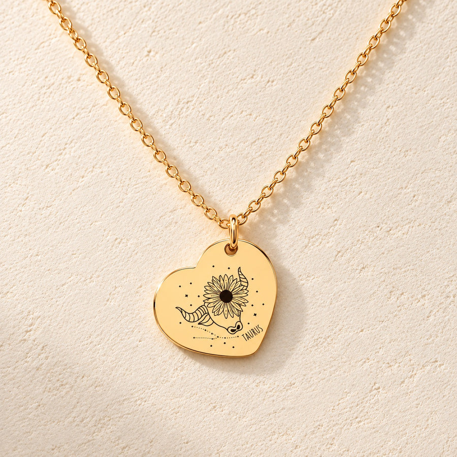 Collier cœur signe astrologique Taureau doré, médaille en cœur gravée avec motif du signe Taureau et ornements, sur fond ivoire.