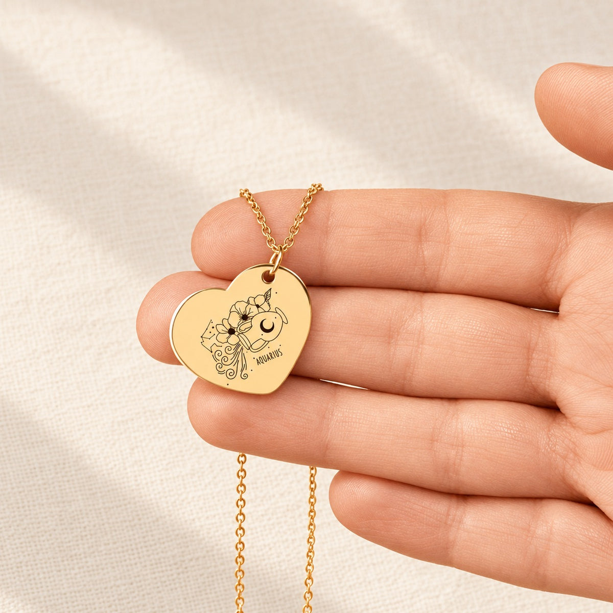 Collier Coeur Signe Astrologique Verseau doré tenu en main, détail de la gravure.