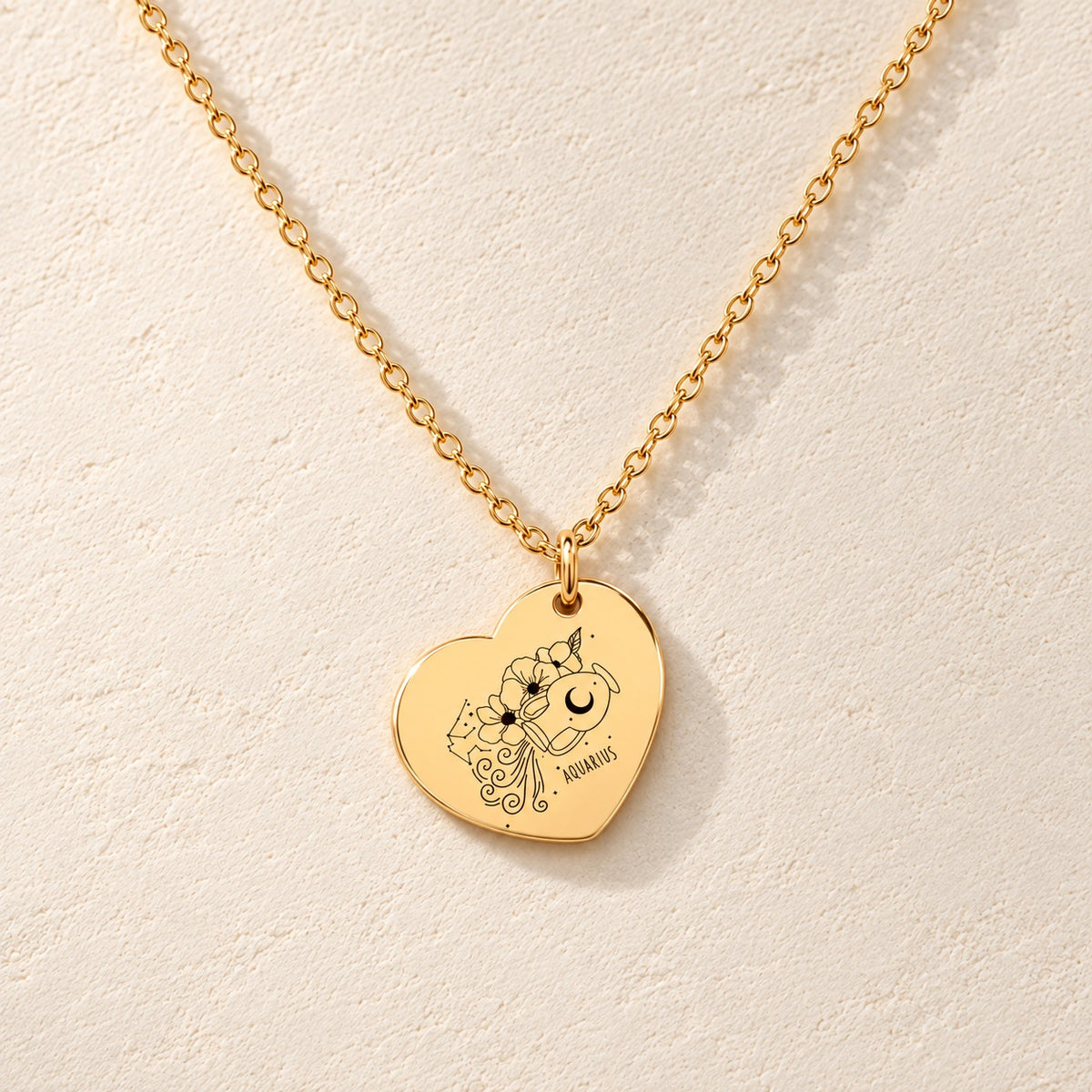 Collier Coeur Signe Astrologique Verseau doré, médaille en cœur gravée avec motif du signe verseau et ornements, sur fond ivoire.