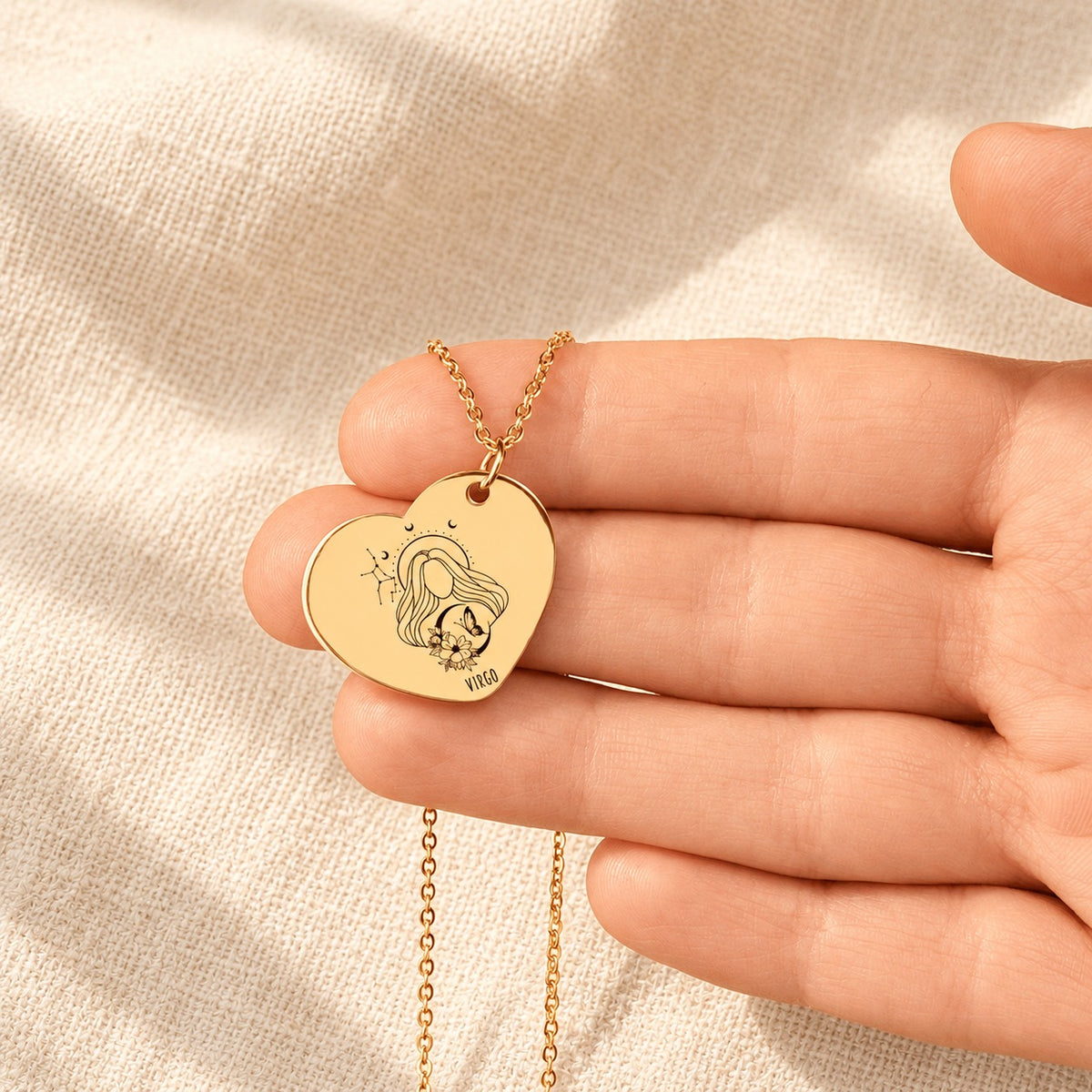 Collier cœur signe astrologique Vierge doré tenu en main, détail de la gravure.