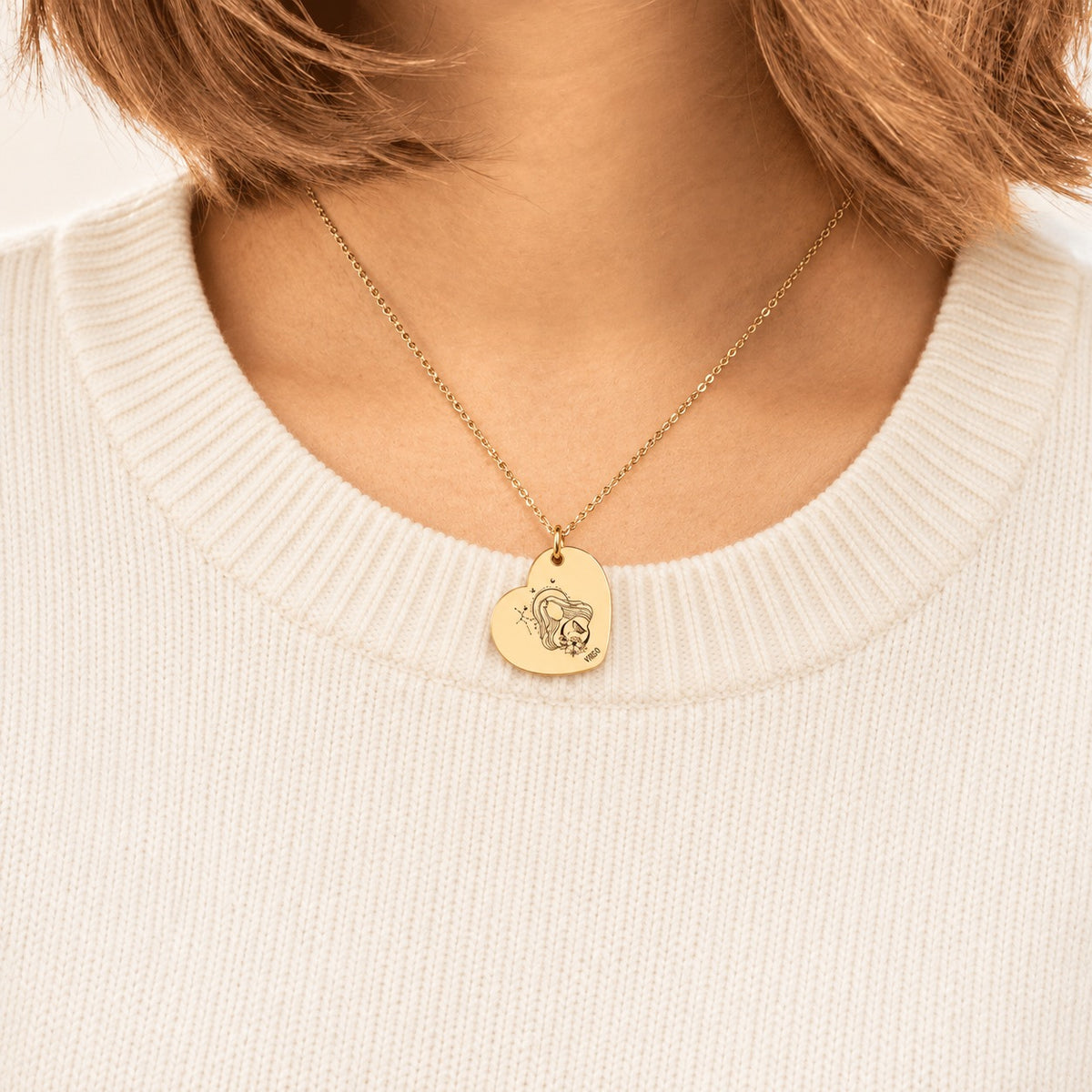 Collier cœur signe astrologique Vierge doré porté au cou, médaille en cœur gravée.