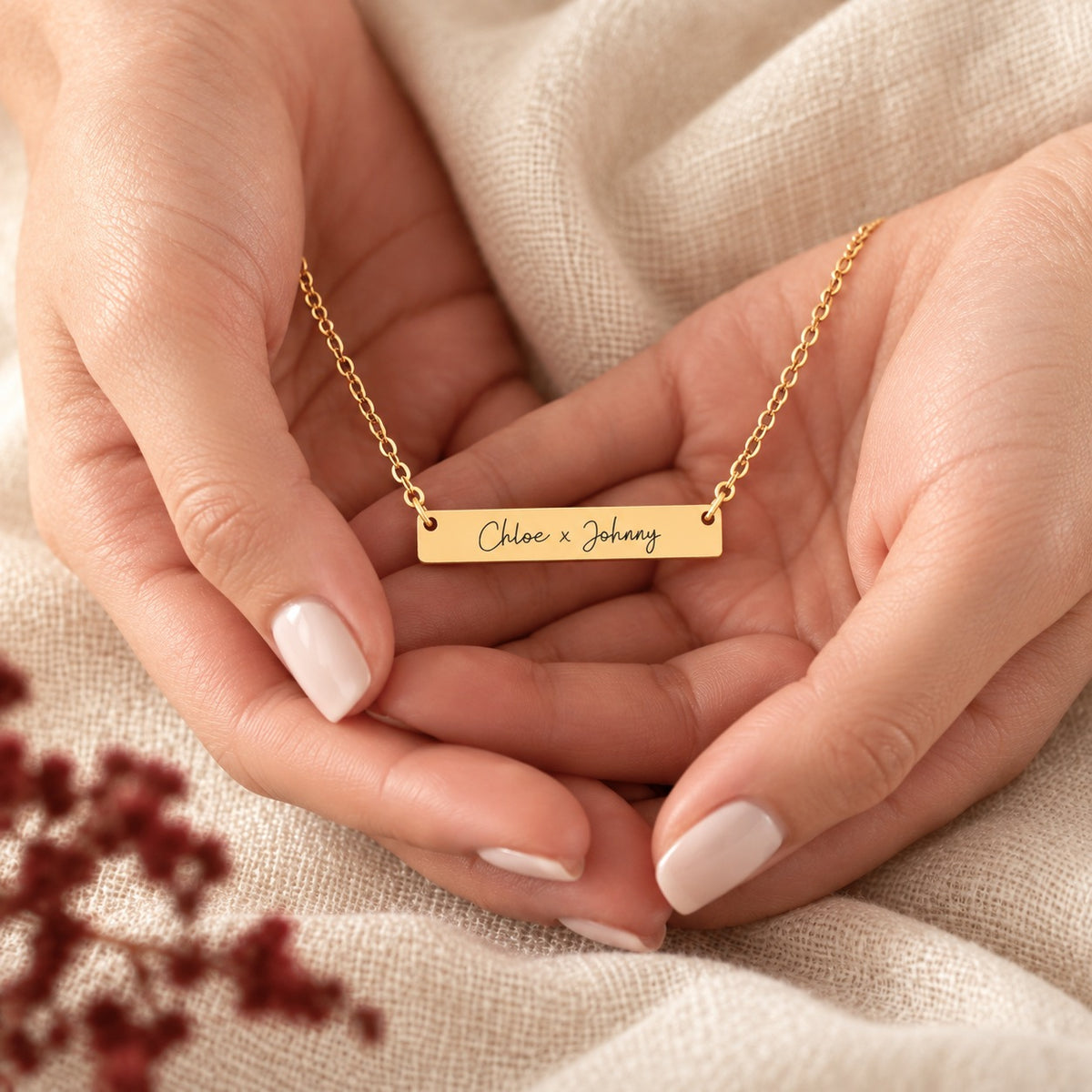 Collier Deux Prénoms doré tenu dans les mains, détail de la barrette et de ses attaches.