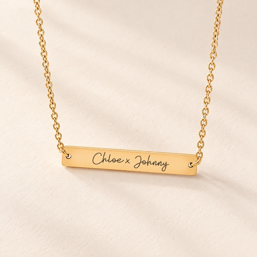 Collier Deux Prénoms doré, barrette gravée Chloe x Johnny sur fond ivoire.