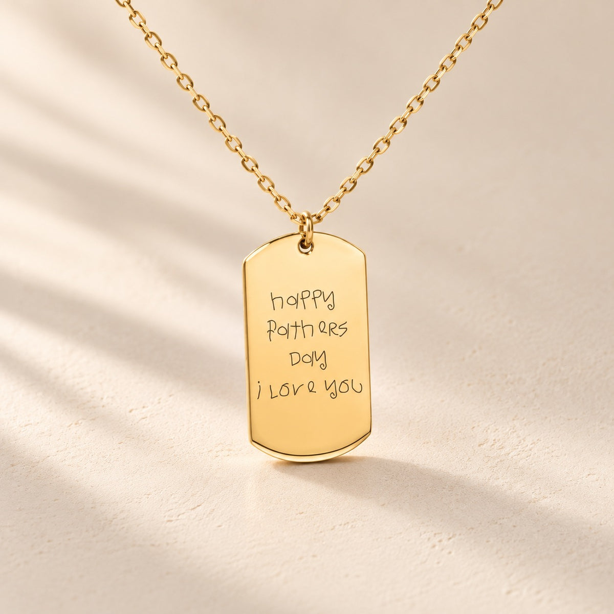 Collier Écriture Manuscrite doré, pendentif rectangulaire avec message d’enfant pour la fête des pères sur fond ivoire.