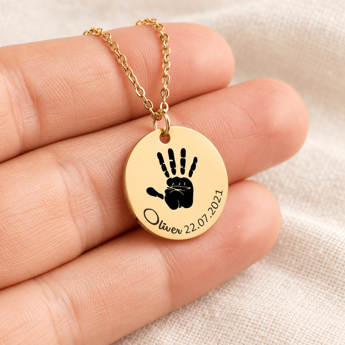 Collier Empreinte de Main doré présenté dans une main, avec médaille ronde gravée.
