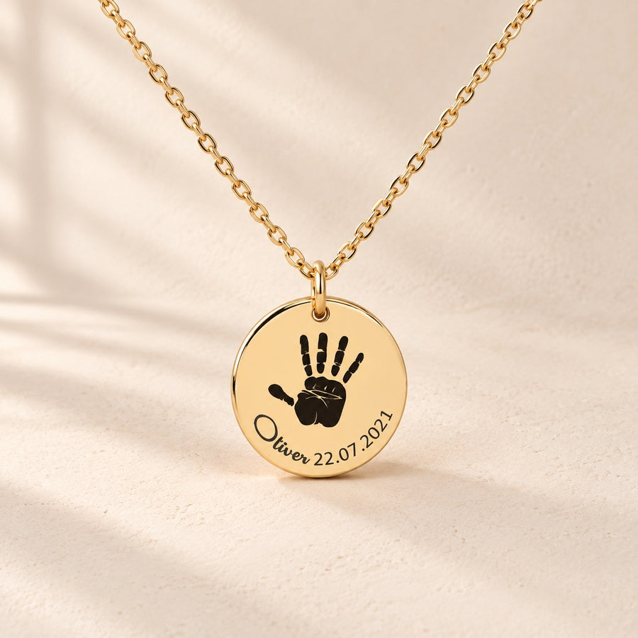Collier Empreinte de Main doré, médaille ronde avec empreinte de main, prénom Oliver et date 22.07.2021 sur fond ivoire.