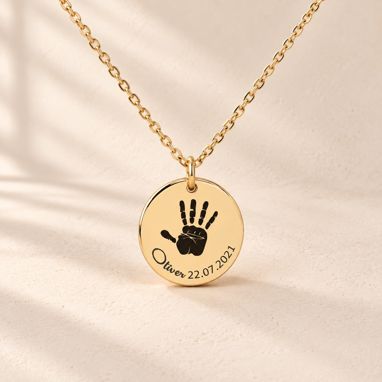 Collier Empreinte de Main doré, médaille ronde avec empreinte de main, prénom Oliver et date 22.07.2021 sur fond ivoire.