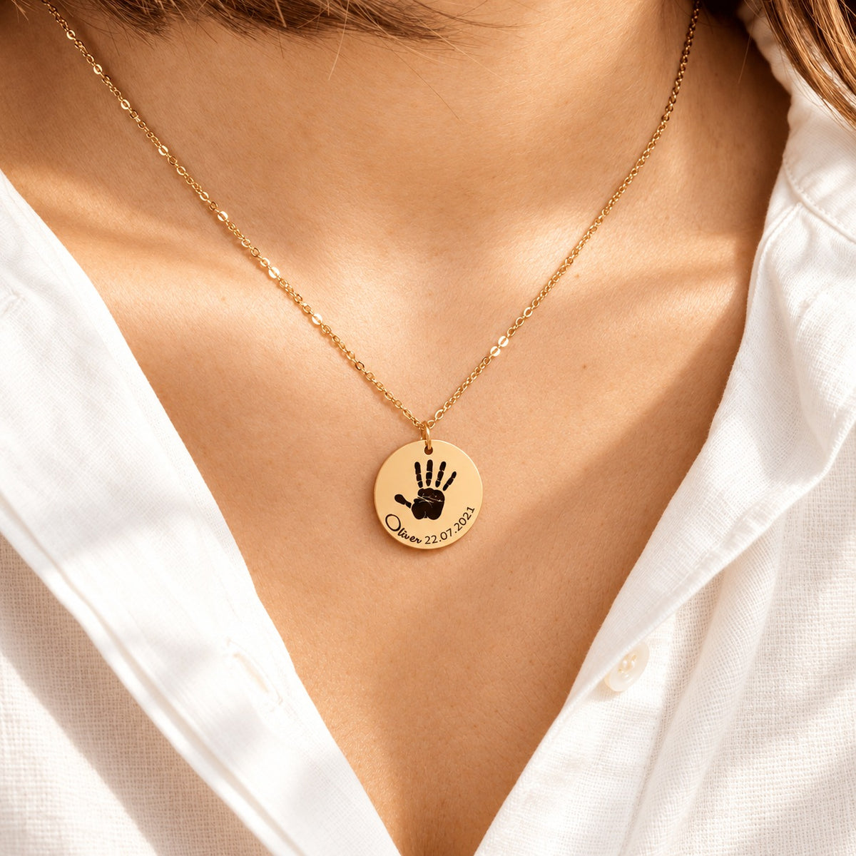 Collier Empreinte de Main doré porté au cou, avec médaille ronde gravée.