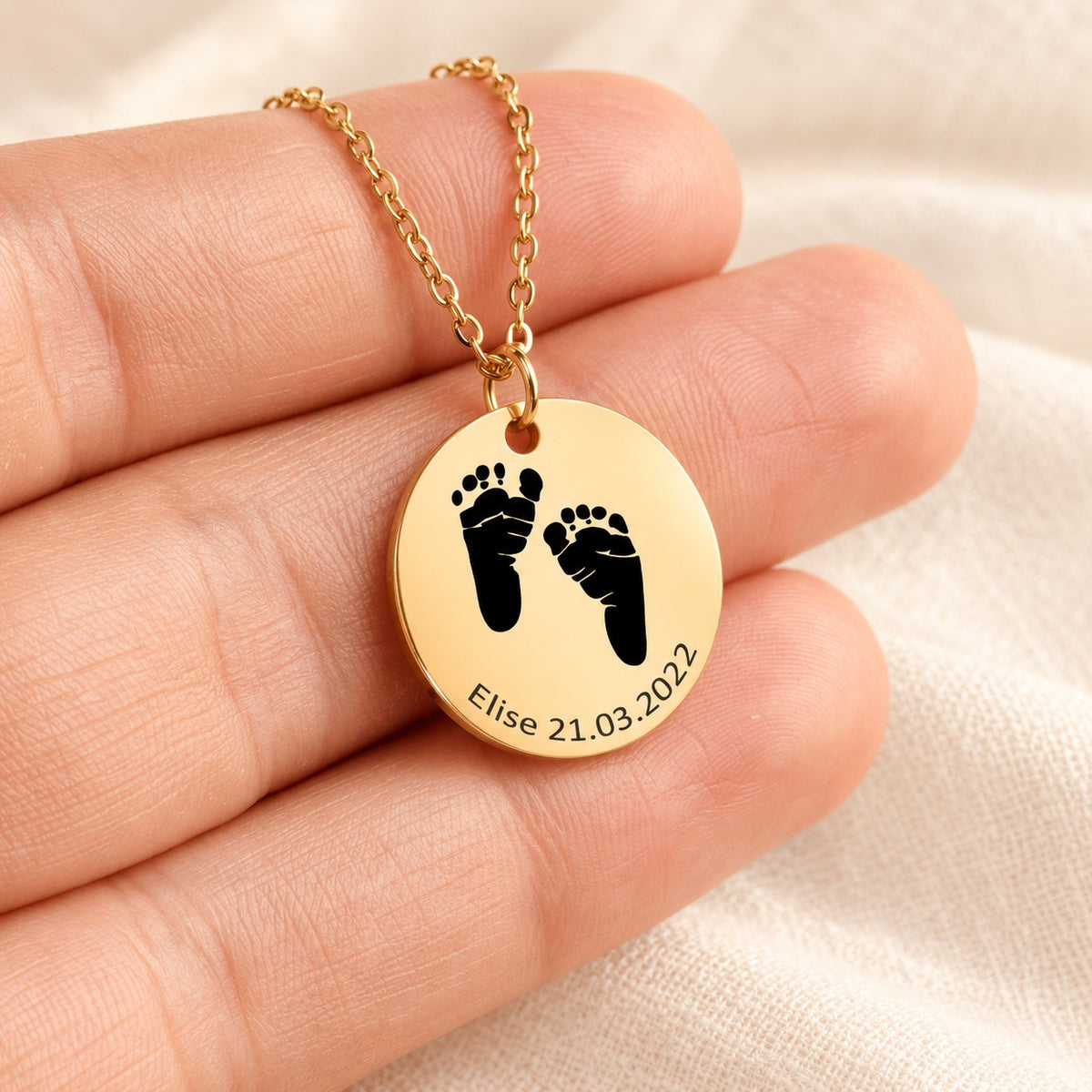 Collier Empreinte de Pied doré présenté dans une main, avec médaille ronde gravée.