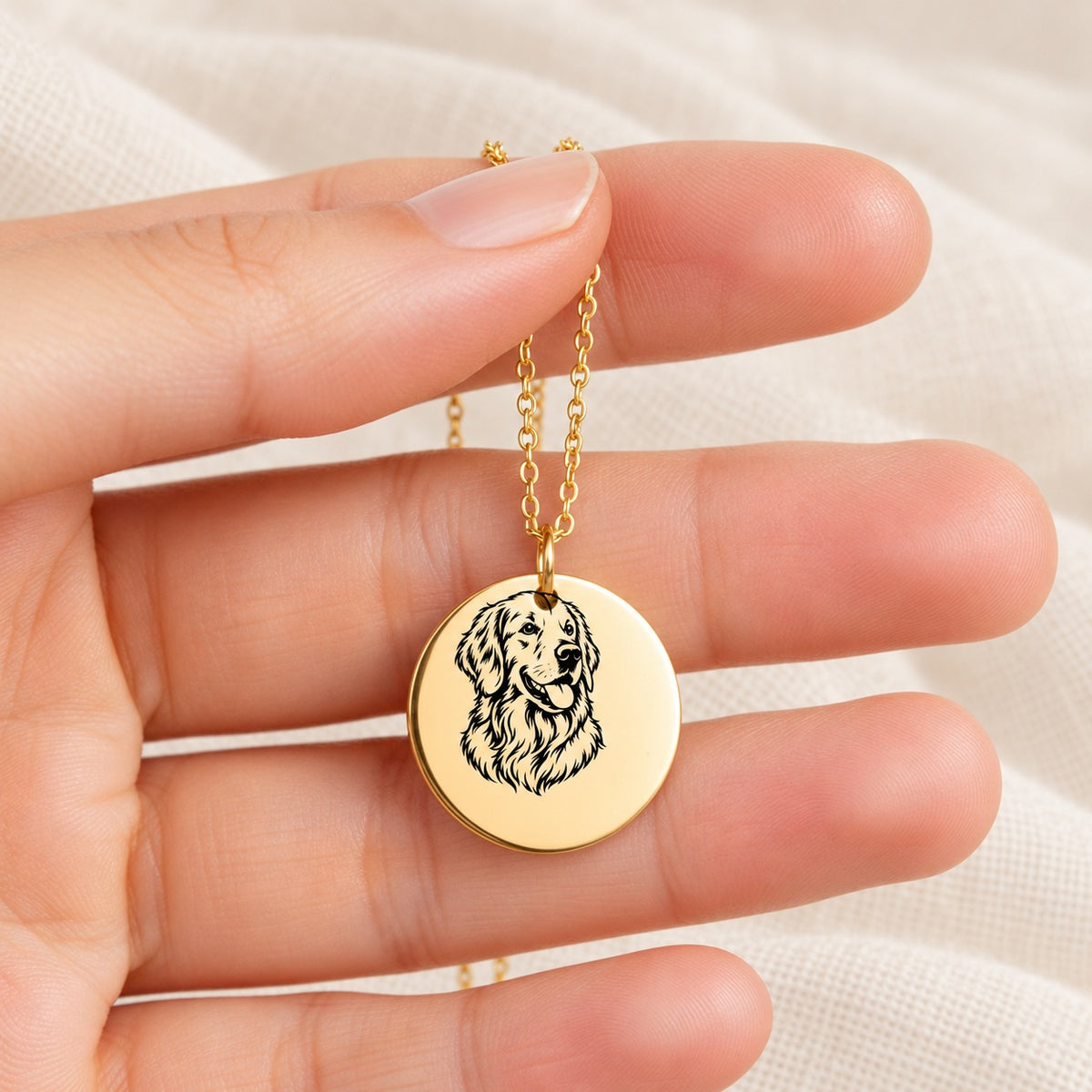 Collier Golden Retriever doré tenu entre les doigts, détail de la médaille et de sa gravure.
