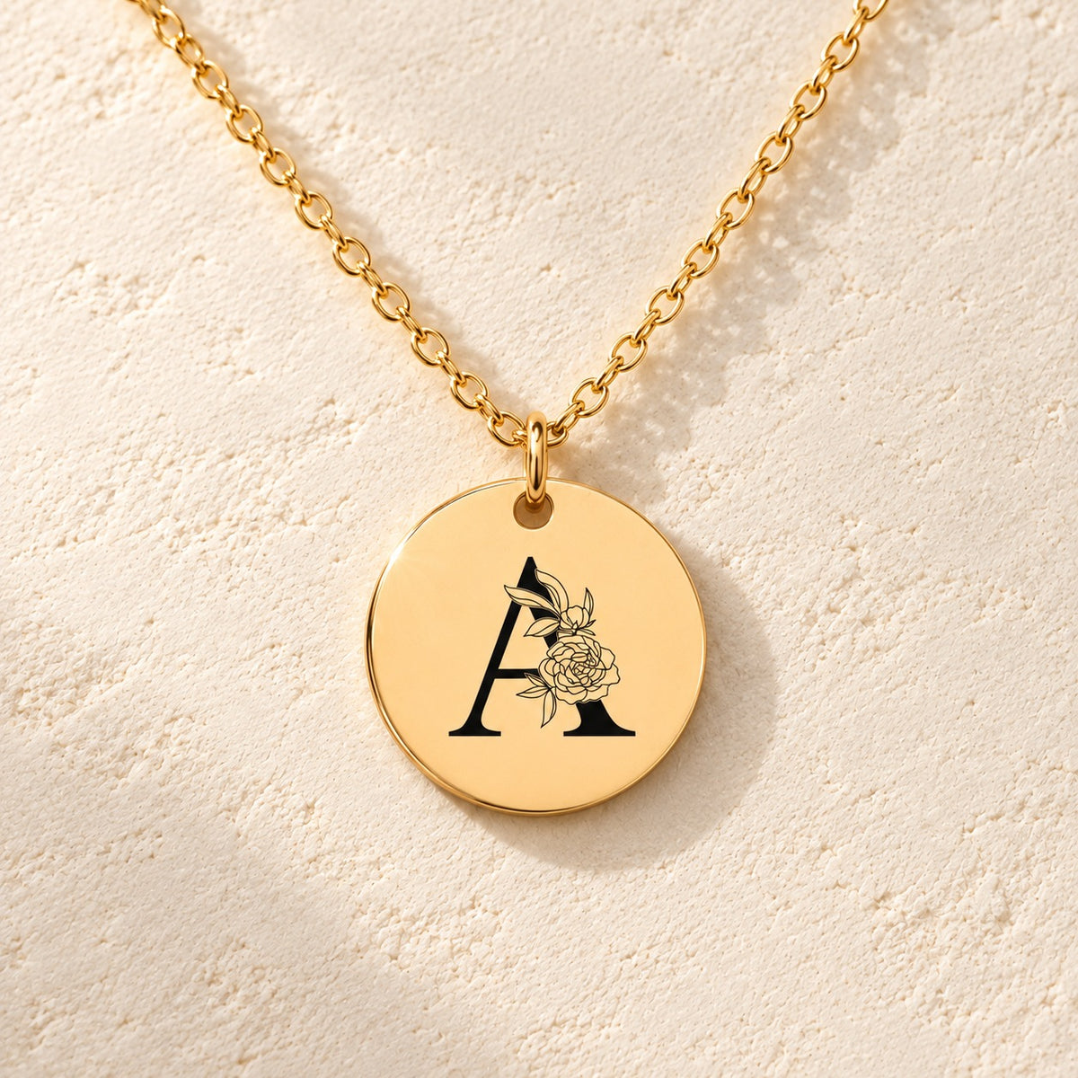 Détail de la médaille ronde dorée avec initiale A et fleurs.