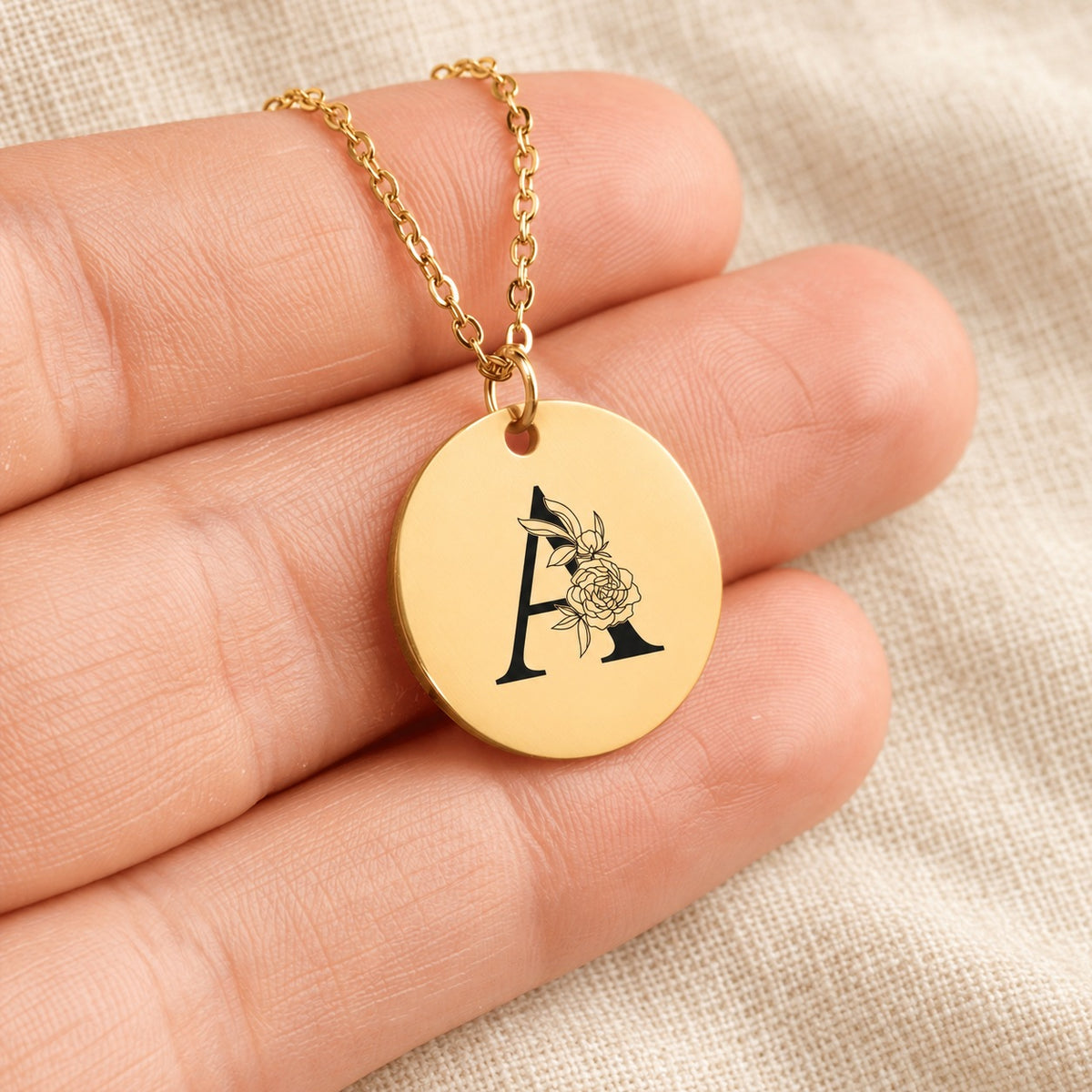 Collier initiale florale A personnalisé doré tenu en main, détail de la gravure.