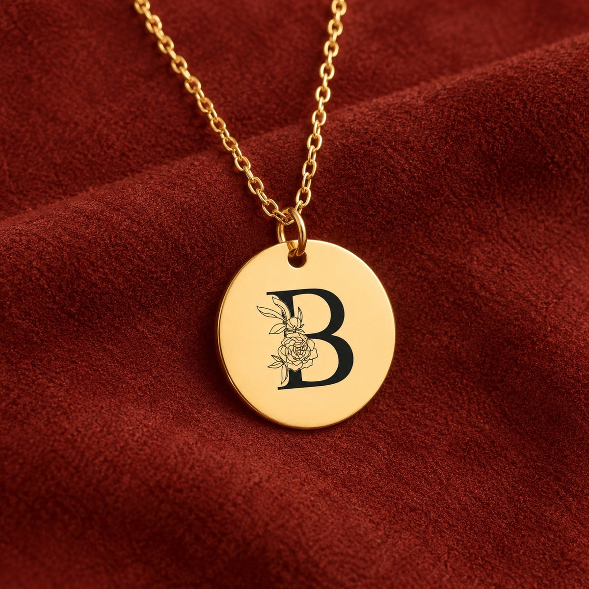 Médaille ronde dorée avec initiale B et fleurs, sur suédine rouge sanguine.