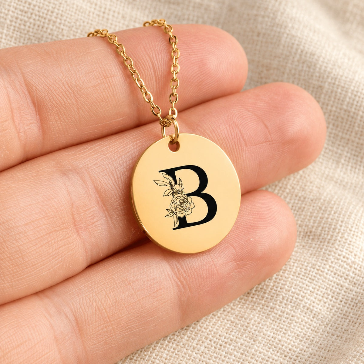 Collier initiale florale B personnalisé doré tenu en main, détail de la gravure.