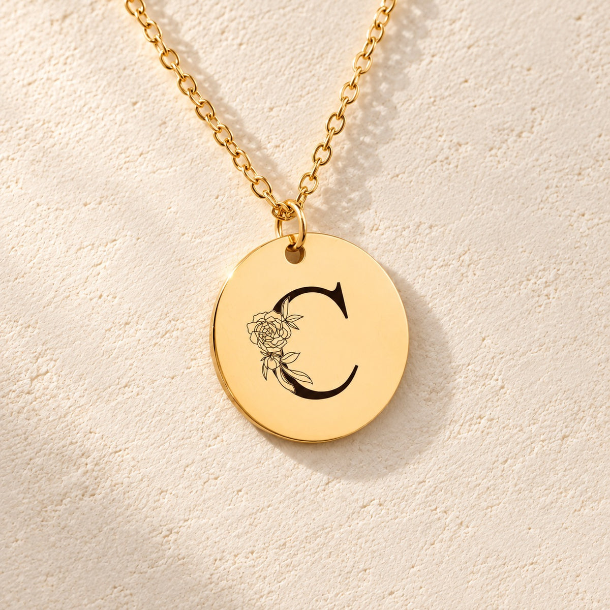 Détail de la médaille ronde dorée avec initiale C et fleurs.