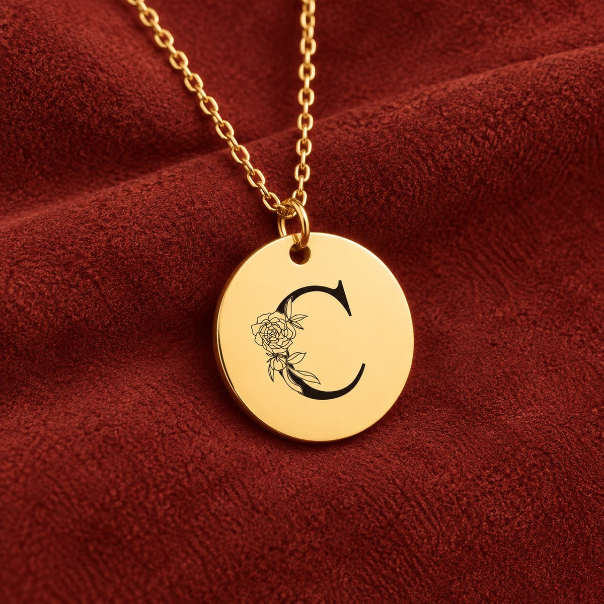 Médaille ronde dorée avec initiale C et fleurs, sur suédine rouge sanguine.