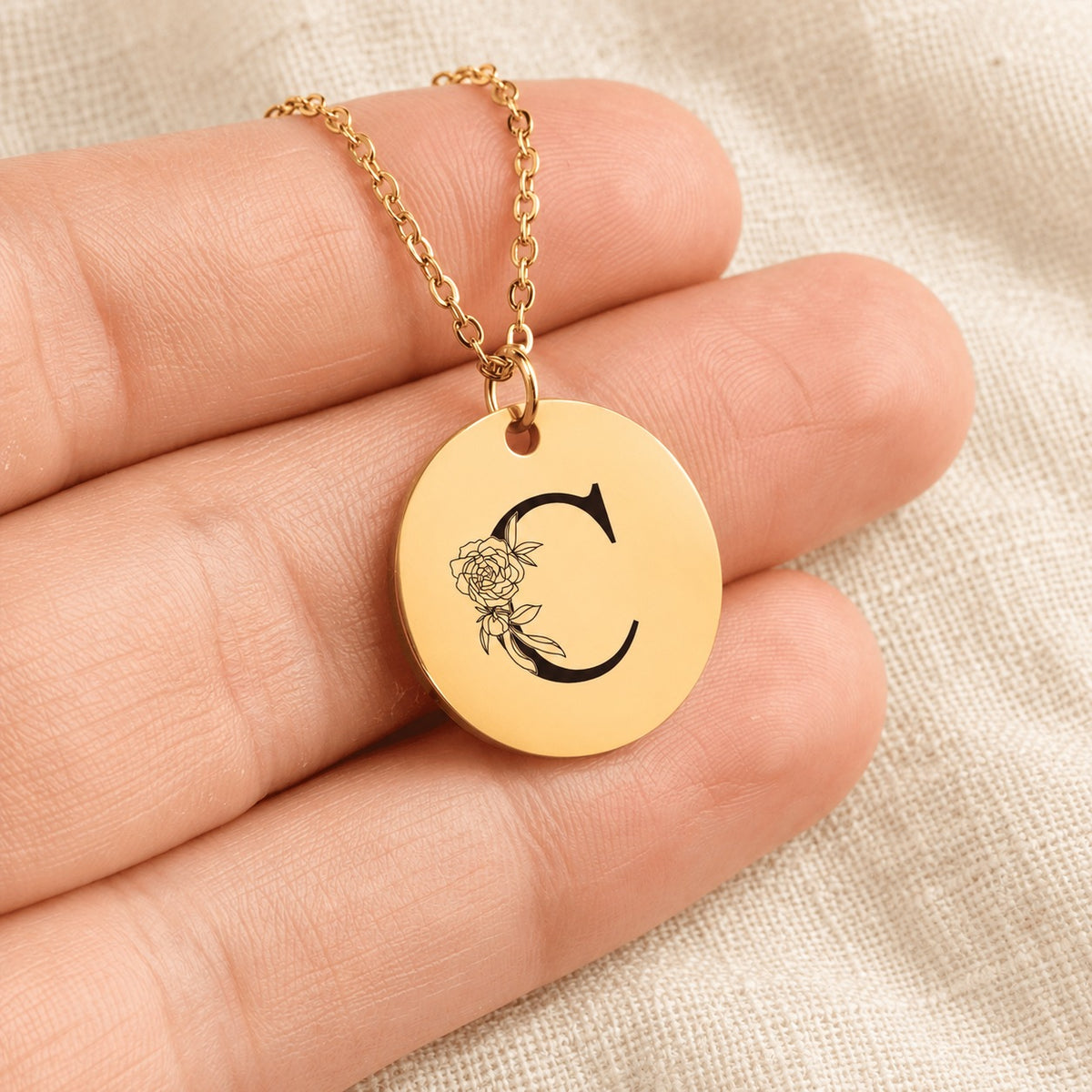 Collier initiale florale C personnalisé doré tenu en main, détail de la gravure.