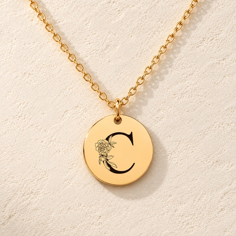Collier initiale florale C personnalisé doré, médaille ronde gravée avec initiale C et fleurs, sur fond ivoire.