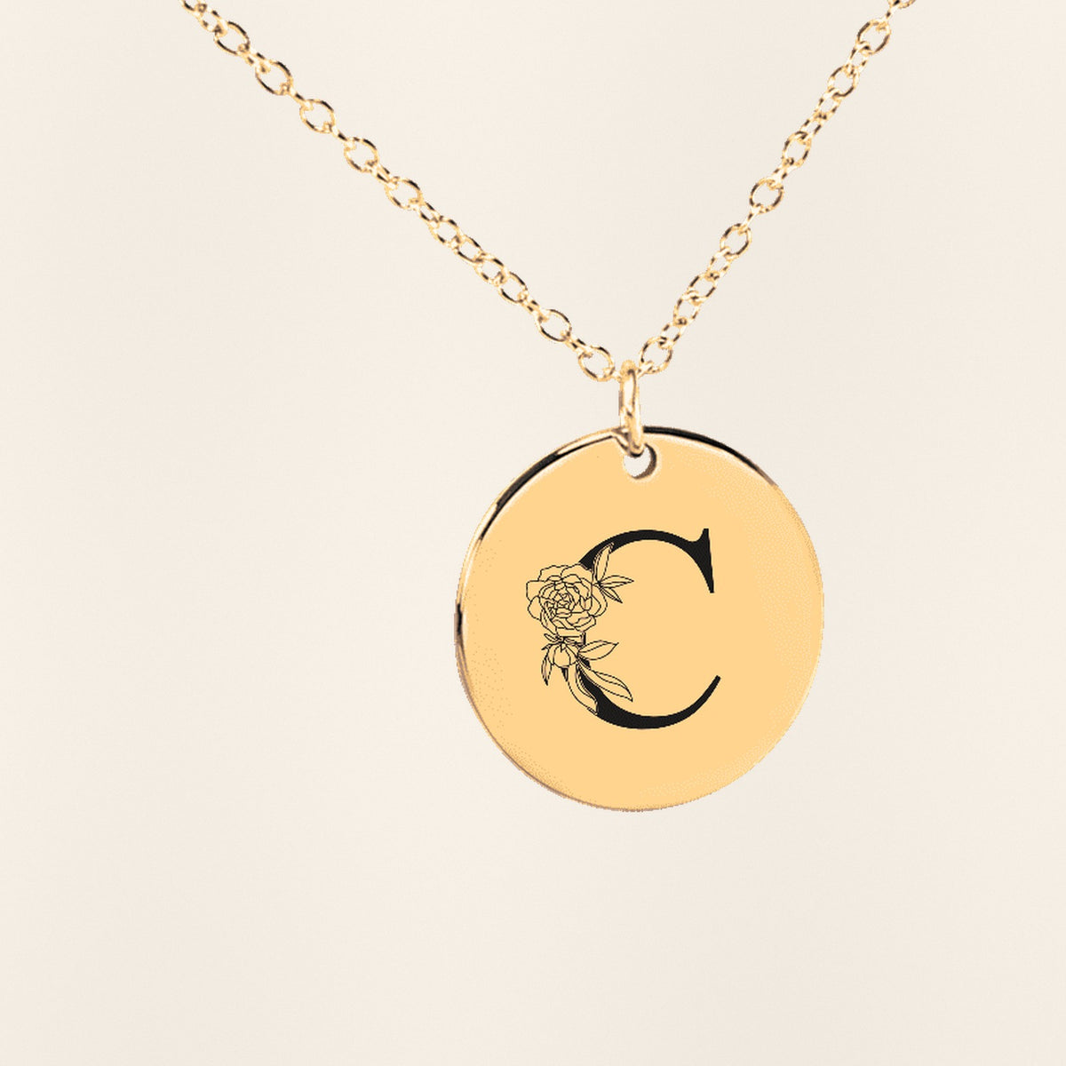 Collier Initiale Florale C Personnalisé en finition dorée, exemple de gravure sur fond ivoire texturé.