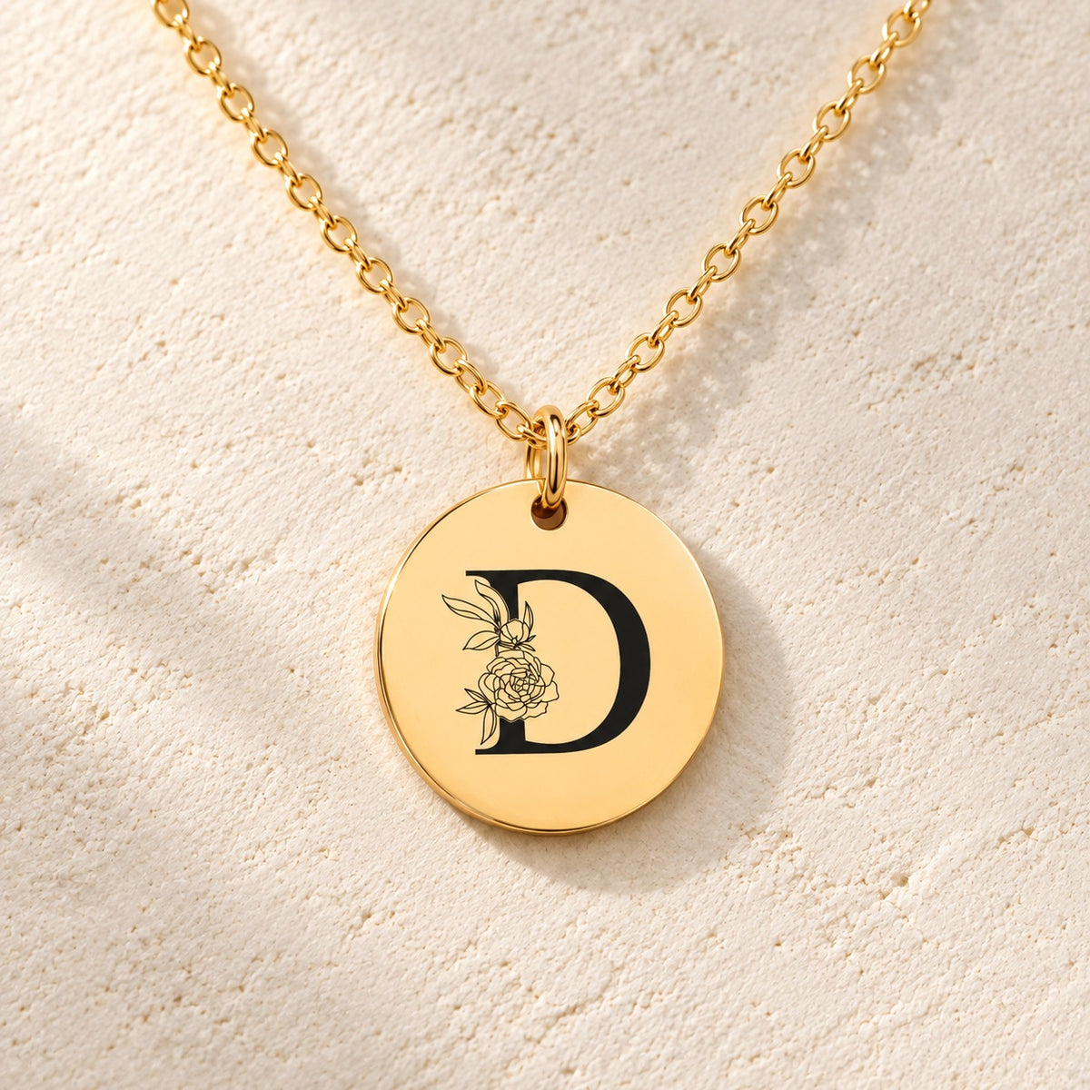Détail de la médaille ronde dorée avec initiale D et fleurs.