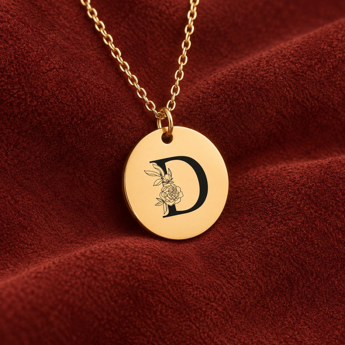 Médaille ronde dorée avec initiale D et fleurs, sur suédine rouge sanguine.