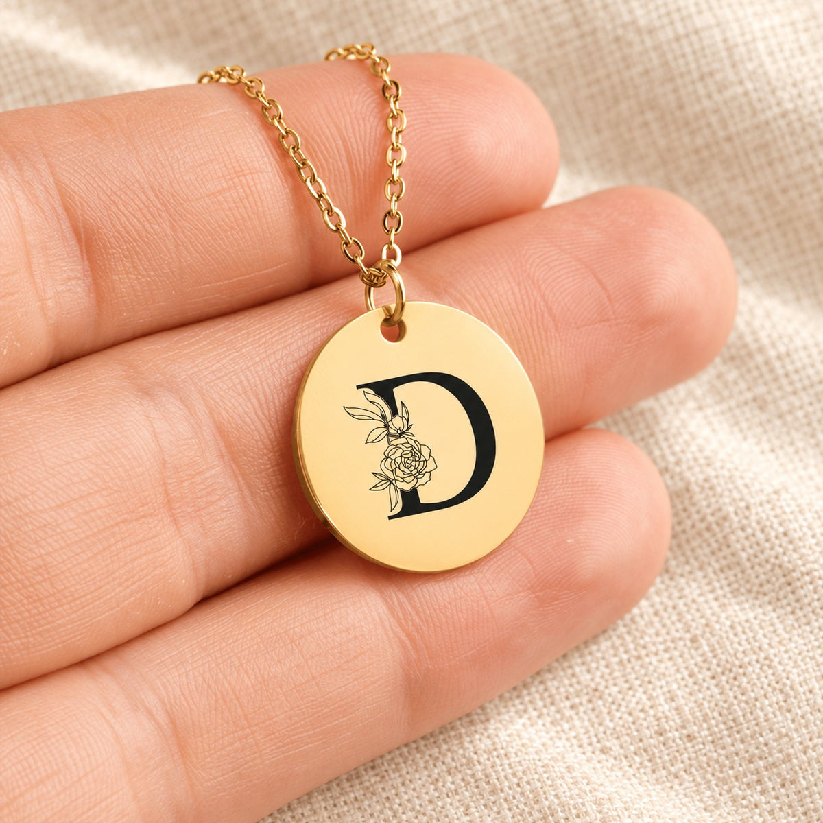 Collier initiale florale D personnalisé doré tenu en main, détail de la gravure.