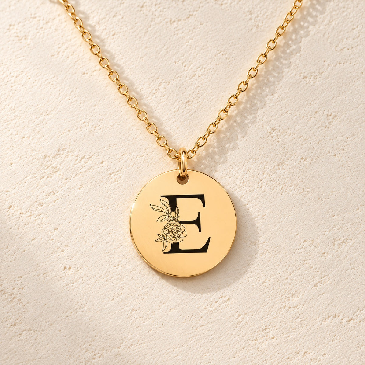 Détail de la médaille ronde dorée avec initiale E et fleurs.