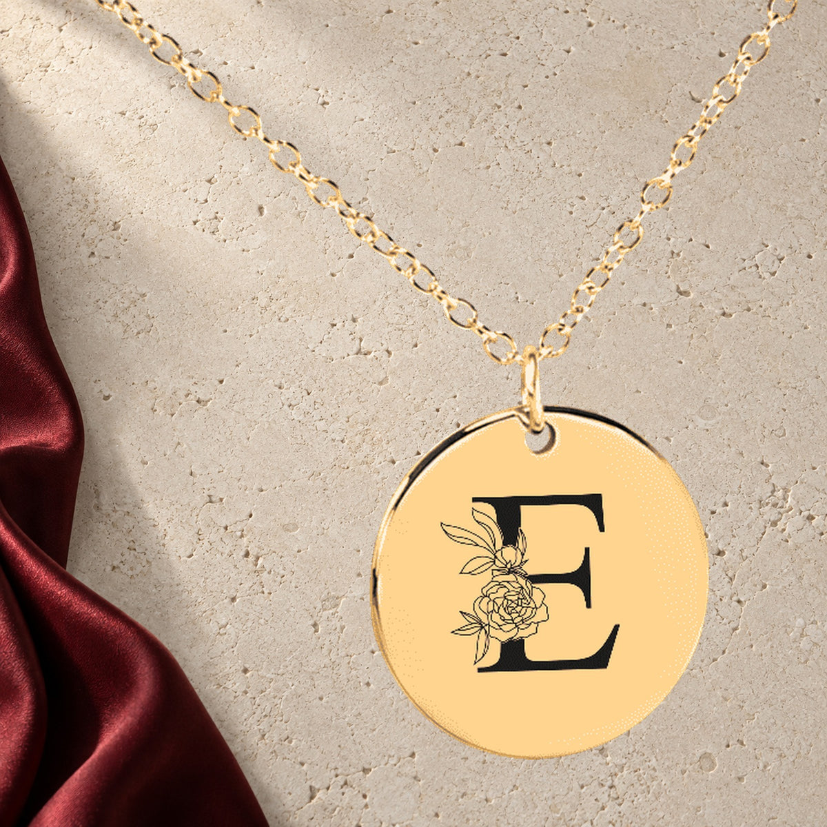 Collier Initiale Florale E Personnalisé en finition dorée sur pierre claire, avec étoffe rouge sanguine ; exemple de personnalisation.
