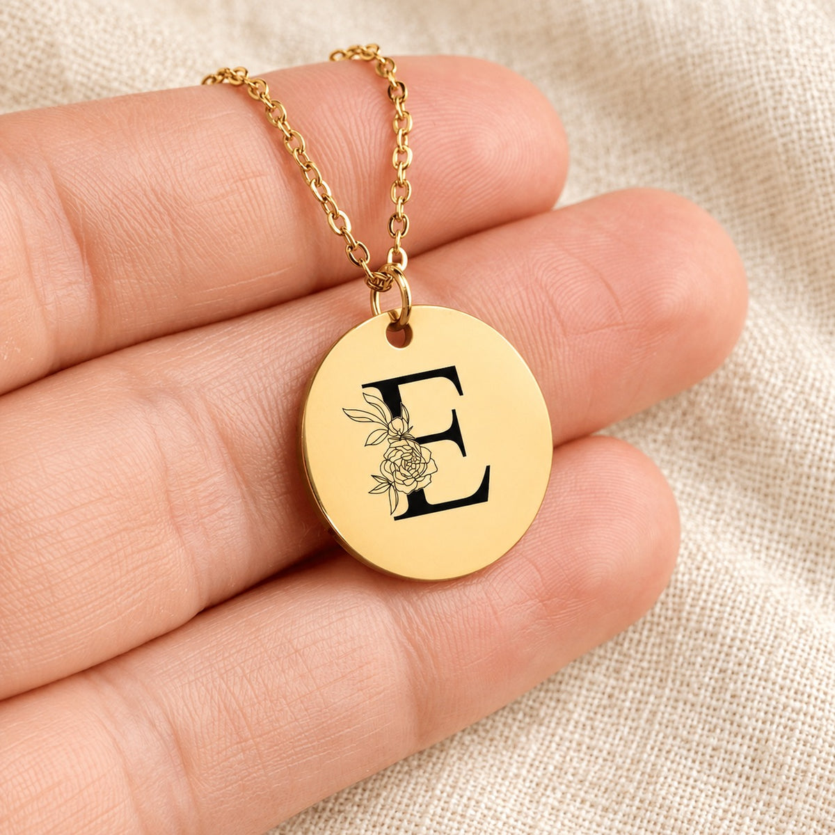 Collier initiale florale E personnalisé doré tenu en main, détail de la gravure.