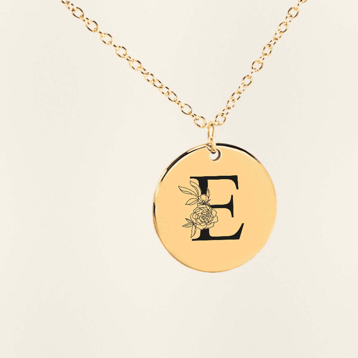 Collier Initiale Florale E Personnalisé en finition dorée, exemple de gravure sur fond ivoire texturé.