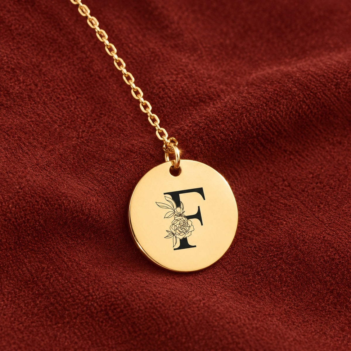 Médaille ronde dorée avec initiale F et fleurs, sur suédine rouge sanguine.